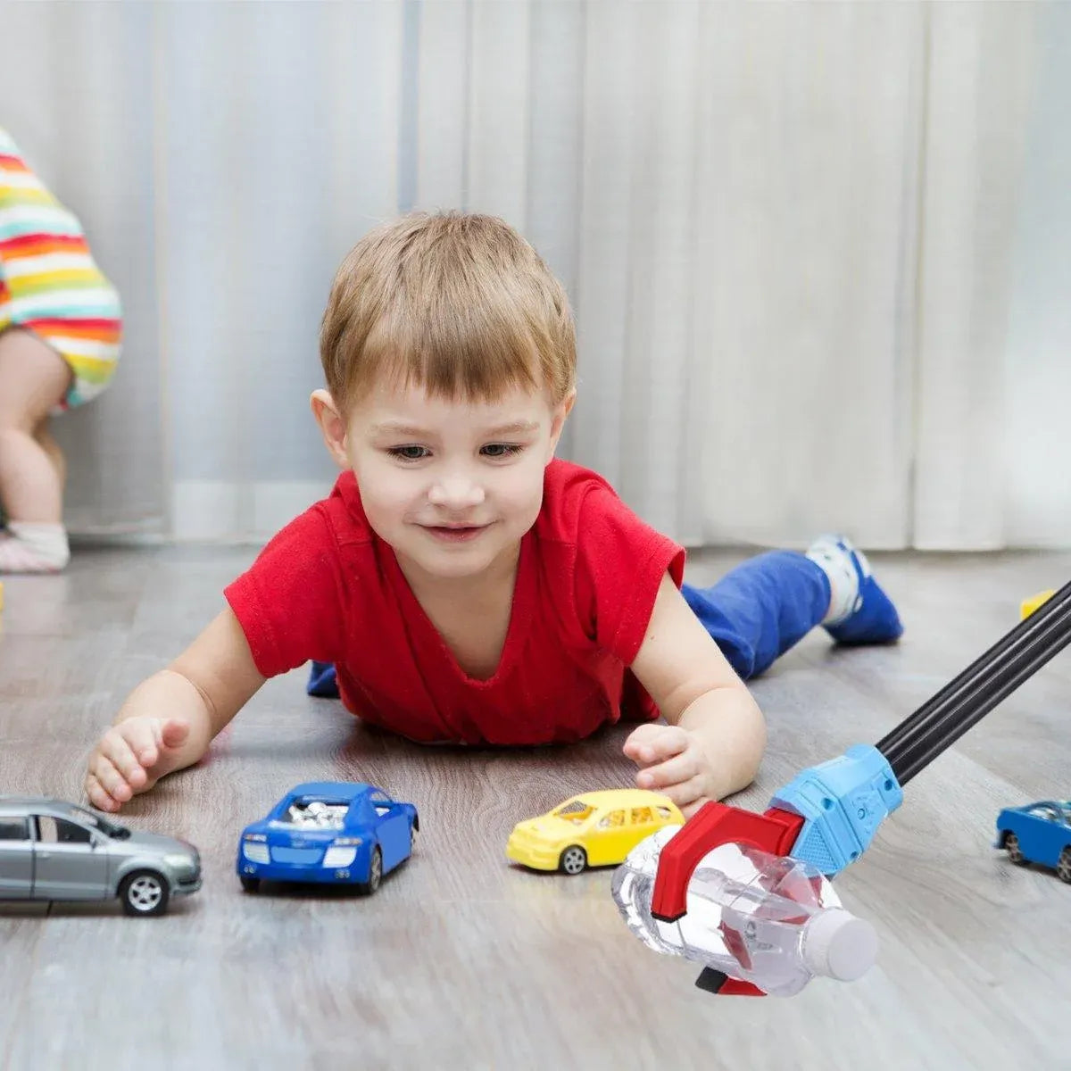 Child playing on the floor beside toy cars and a robot claw holding a bottle