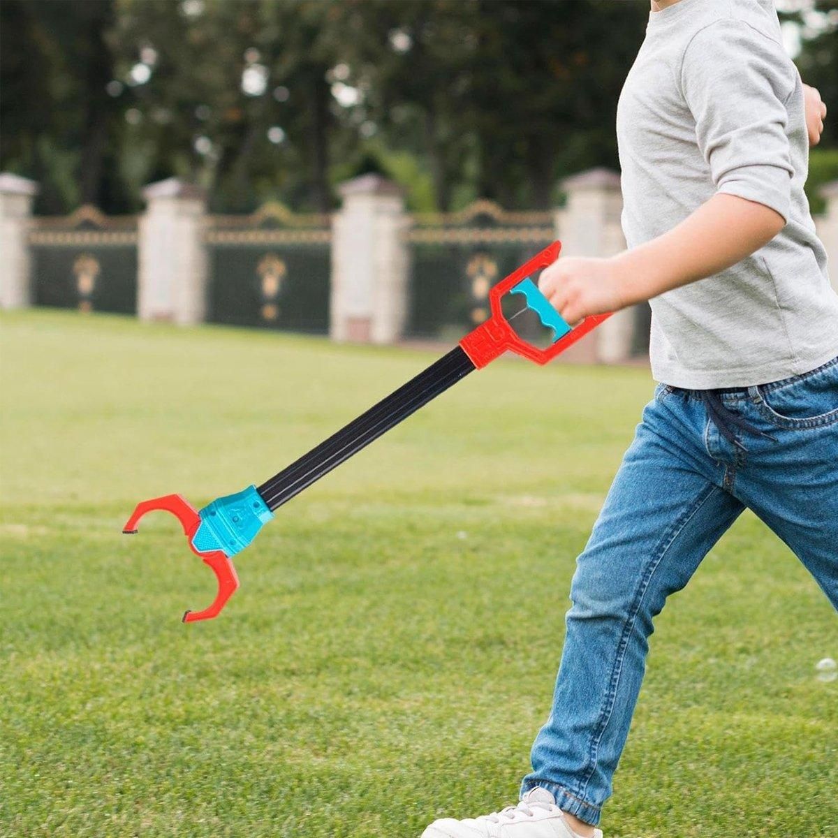 Child outdoors holding a red-handled robot claw grabber over the lawn