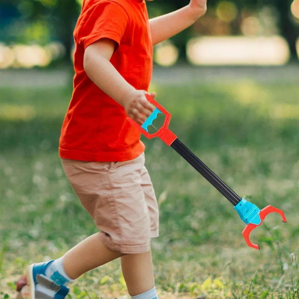 Child walking on grass while carrying a robot claw grabber